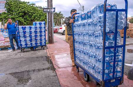 Empleados de un supermercado descargan botellas de agua para abastecer a sus clientes por la llegada del huracán Dorian.