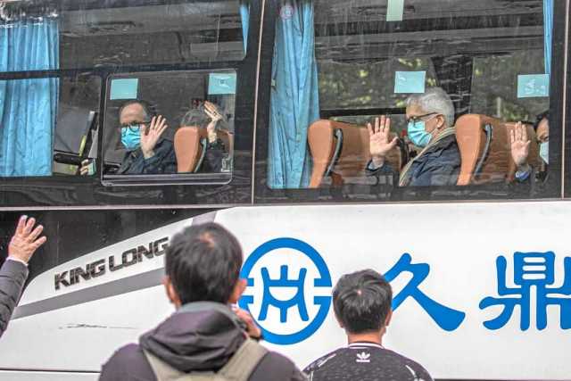 El equipaje de los expertos fue cargado en el autobús por trabajadores cubiertos con trajes de protección blancos, mascarillas y