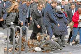 El presidente francés, Emmanuel Macron, pasa junto a una motocicleta calcinada, tras las protestas del sábado. 