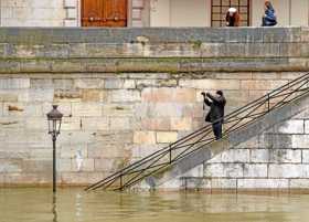 Un hombre toma una fotografía de una farola rodeada de agua en Ile Saint-Louis, a orillas del río Sena en París, Francia.