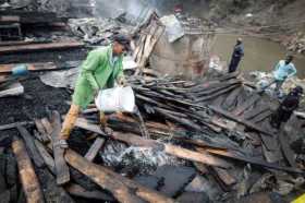 Un hombre echa agua sobre madera quemada tras un incendio en el mercado Gikomba en Nairobi (Kenia)