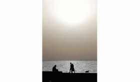 Una familia descansa este miércoles junto al mar mientras atardece entre la nube de polvo del Sahara que por estos días atravies