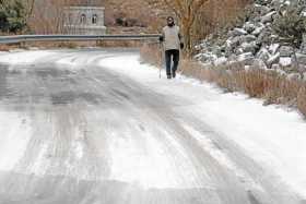Un hombre pasea por un tramo de la carretera de acceso al embalse de Fuentes Claras con placas de hielo por las bajas temperatur