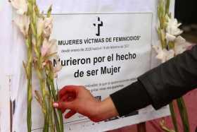 Una persona coloca una flor cerca de un cartel en honor a las víctimas de feminicidios durante el acto simbólico denominado "Viv
