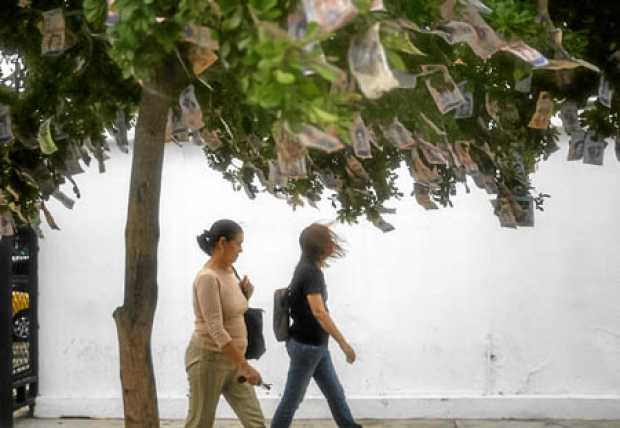 Dos mujeres caminan junto a un árbol con billetes venezolanos en sus ramas en Maracaibo. 