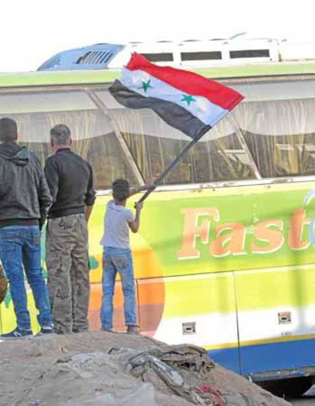 Un niño ondea una bandera siria mientras autobuses del gobierno, con decenas de combatientes del Ejército al Islam a bordo, sale