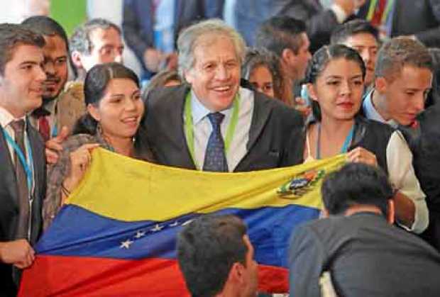 El secretario general de la OEA, Luis Almagro, posa para una foto con dos jóvenes venezolanas y una bandera de ese país.