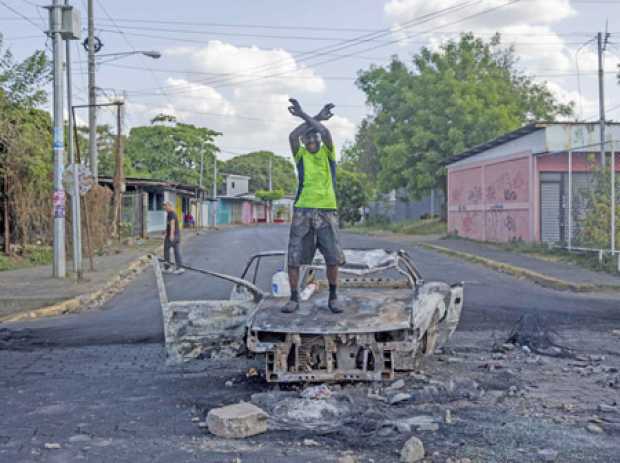 Un hombre protesta encima de un vehículo quemado.