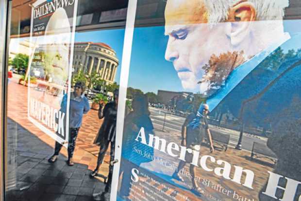 Los peatones se reflejan en la página principal de Fayetteville Observer y NY Daily News, que conmemoran al senador republicano 