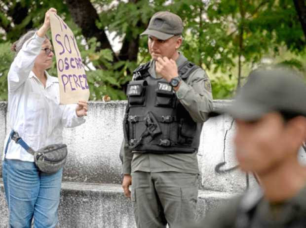 Una mujer sostiene un cartel en el que se lee "Yo soy Óscar Pérez", frente a miembros de la Guardia Nacional y la Policía Nacion