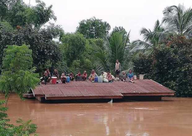 Personas aguardan en lo alto de un tejado en una zona inundada tras el derrumbe de una presa hidroeléctrica en un pueblo cercano
