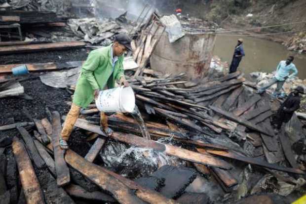 Un hombre echa agua sobre madera quemada tras un incendio en el mercado Gikomba en Nairobi (Kenia)