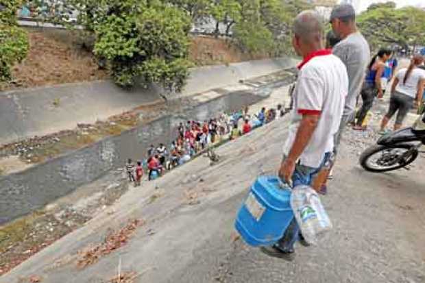 Personas recogen agua, en la autopista Francisco Fajardo, en Caracas. El apagón que sufre Venezuela no permite la llegada de agu