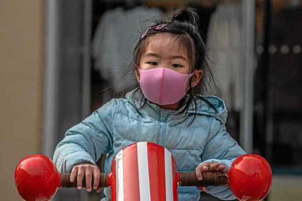 Una niña con una mascarilla facial sanitaria juega en un parque de una desértica área comercial en Solana, Pekín (China).